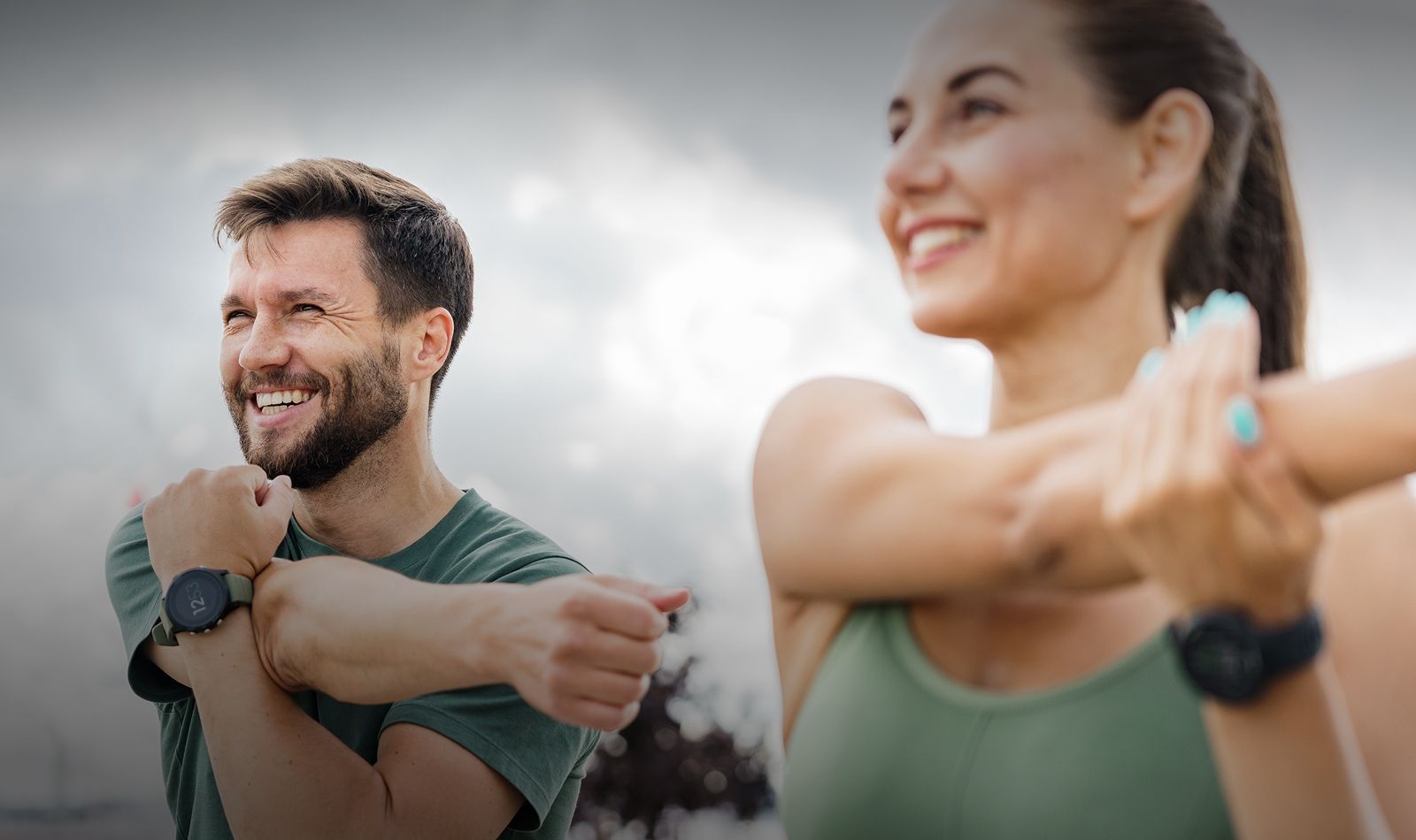 Smiling individuals stretching during outdoor exercise.